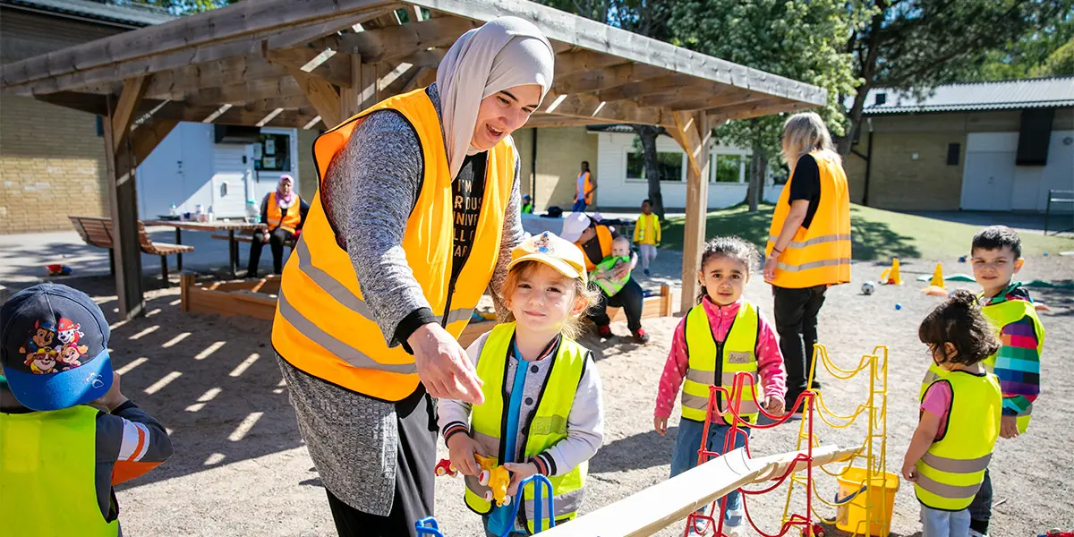 Flera små barn är ute tillsammans med förskollärare på förskolans skolgård.