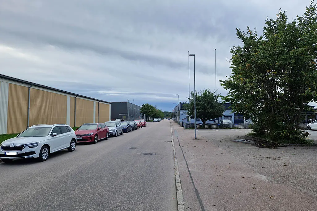 Bilden visar en gata med parkerade bilar längs ena sidan av gatan.