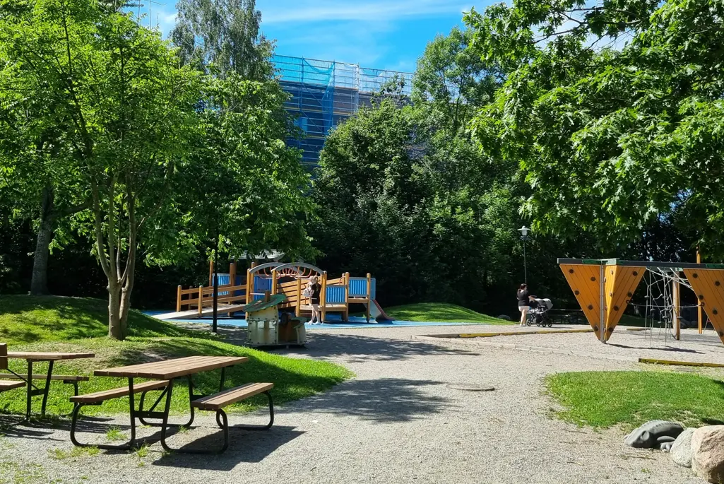 Lekplats med lekställningar omgivna av träd. 