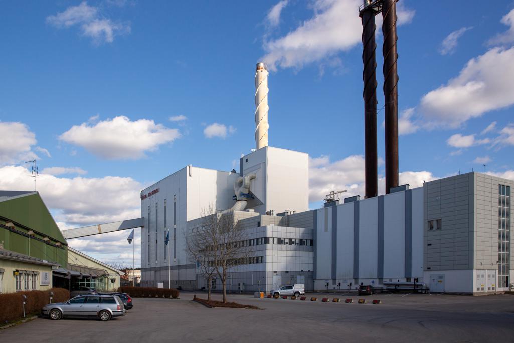 Stor vit industribyggnad med skorstenar. Det står en bil parkerad framför byggnaden.