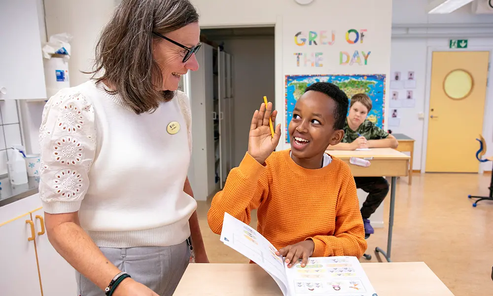 Bild på elev som sitter vid sin bänk och får hjälp av en pedagog.