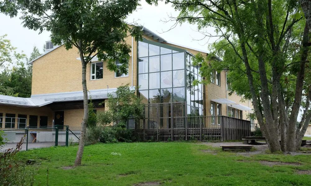 Foto på Skolstaskolan. Det är en stor gul tegelbyggnad med stora glasfönster. 