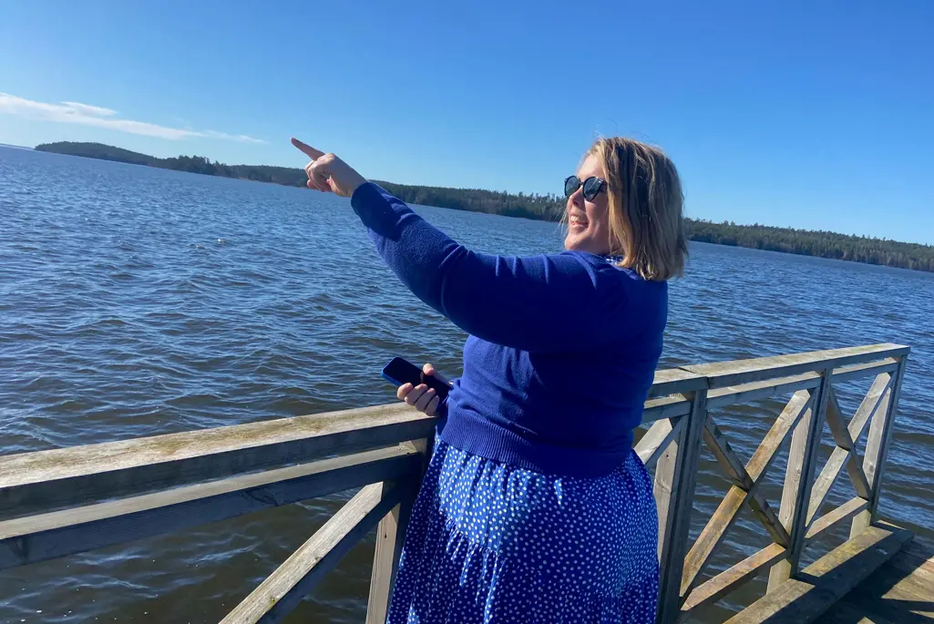 Foto på en kvinna klädd i blått som står på en brygga vid vattnet och pekar.