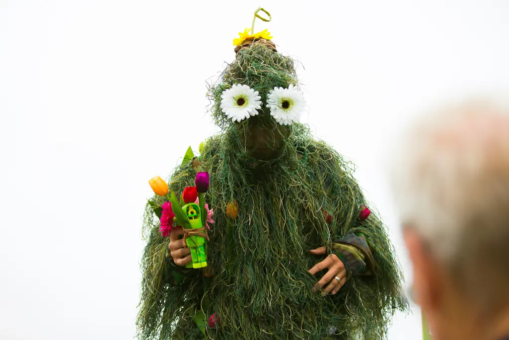 Foto på en person utklädd i gräs och blommor till ögon.