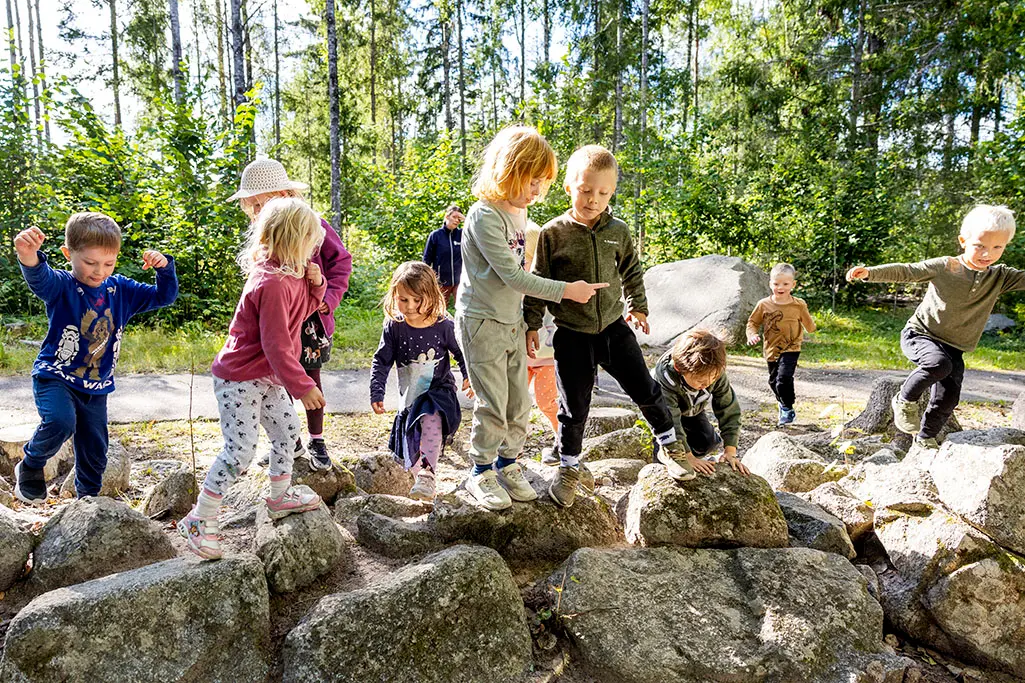 Foto på flera barn som gungar. En vuxen person står i bakgrunden.